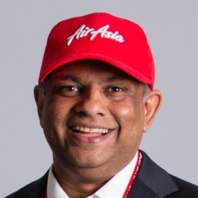 A smiling darker-skinned male wearing a red baseball cap with a dark gray suit against a gray background