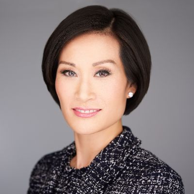 A smiling female of Asian heritage with short black hair wearing a tweed black blazer against a gray background