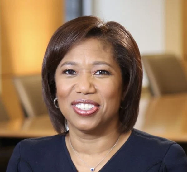 A smiling darker-skinned female with short brown hair wearing a navy shirt against an ambiguous background