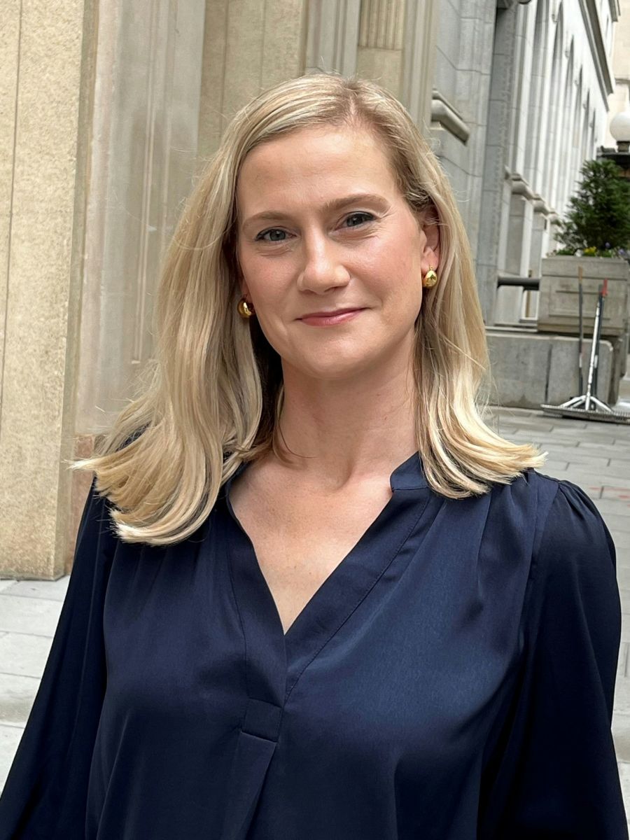 A smiling light-skinned female with blonde hair wearing a navy blue shirt against an ambiguous background