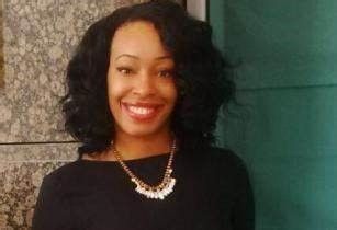 A smiling darker-skinned female with short black hair wearing a black shirt against an ambiguous background