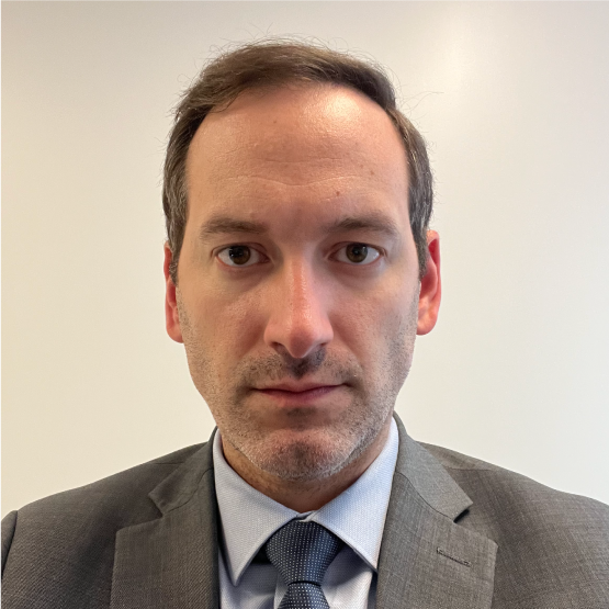 A light-skinned male with short brown hair wearing a gray suit and tie against a light background