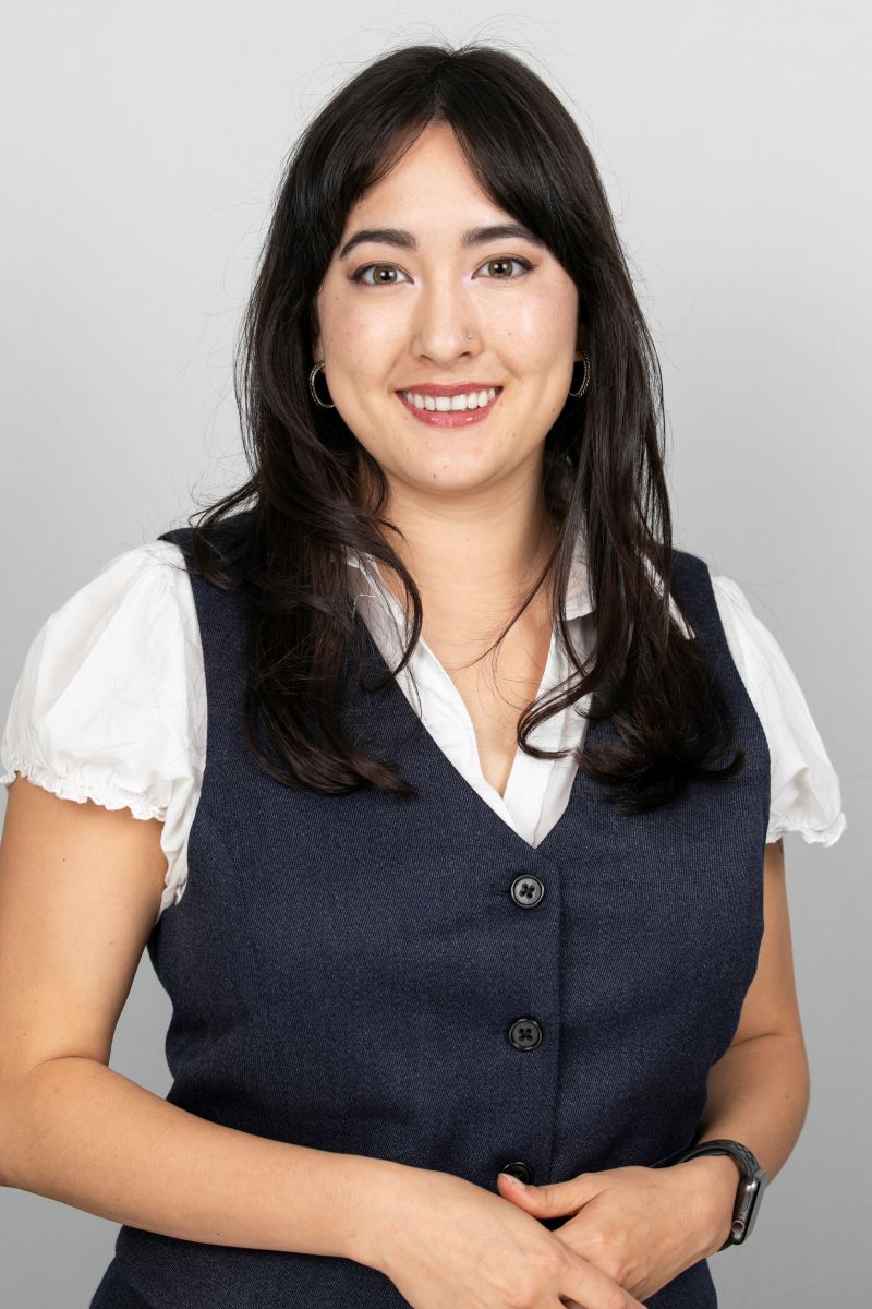 A woman wearing a white shirt and navy vest against a light background.