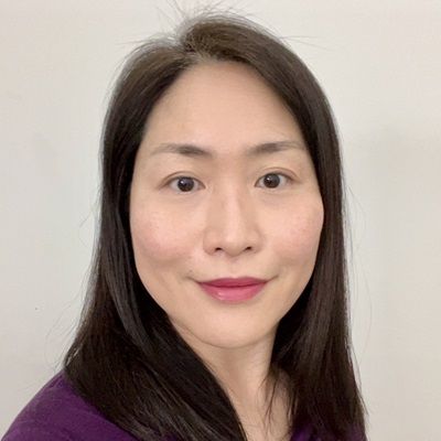 A smiling woman of Asian heritage with long black hair wearing a purple shirt against a white background