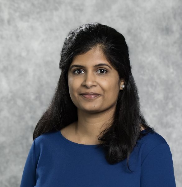 person with long dark hair pulled half back, wearing medium blue shirt, partially smiling