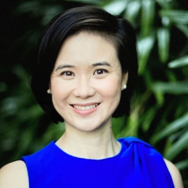 A headshot of an adult woman who is Asian in appearance. She is smiling at the camera, wearing a royal blue top, and she has bobbed black hair and brown eyes. 