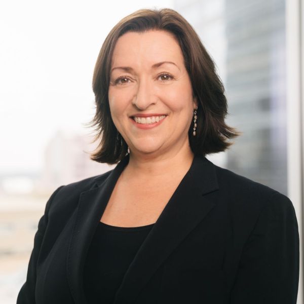 A headshot of an adult woman wearing all black and smiling at the camera. She has shoulder-length brown hair and brown-ish eyes.