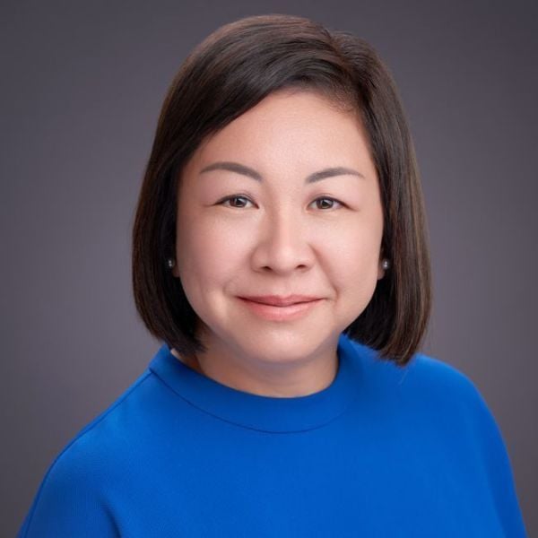 A headshot of an adult woman who is Asian in appearance and smiling at the camera. She has brown-black hair in the style of a long bob and she is wearing a royal blue sweater.