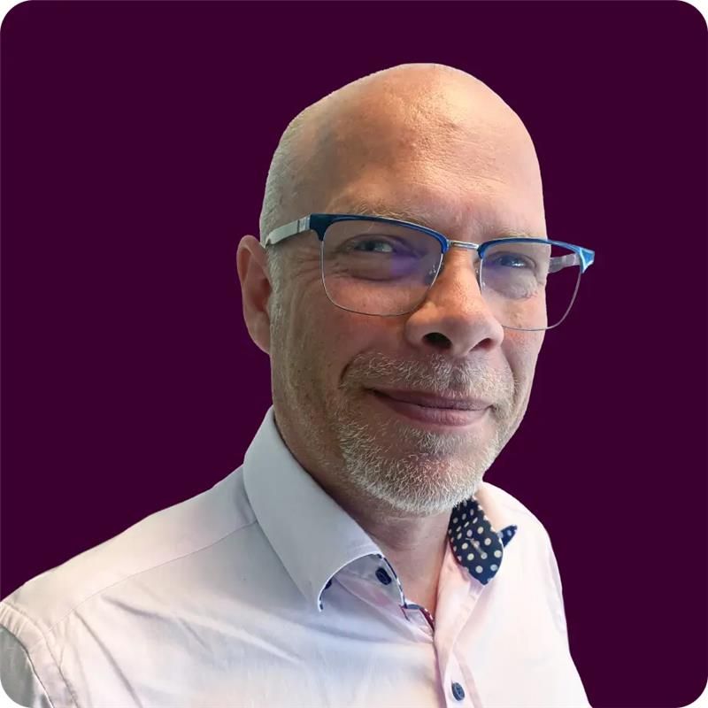 A headshot of an older adult man named Matt Bonam. He is bald with pale white skin, a stubbly beard, and wearing glasses and a pink collared shirt.