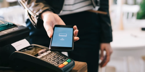 Person holds mobile phone in front of a card reader for payment