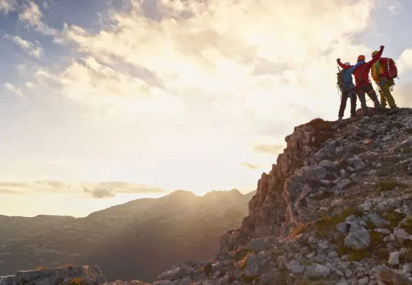 three people at the top of a mountain, one with arms raised