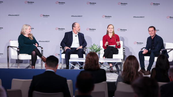 An image of four adults, two men and two women, all with white skin, sitting on a stage and talking. The backdrop reads "Reuters, The Source" and "#ReutersNext".