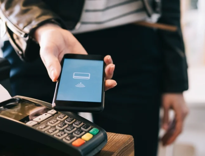 Person holds mobile phone in front of a card reader for payment