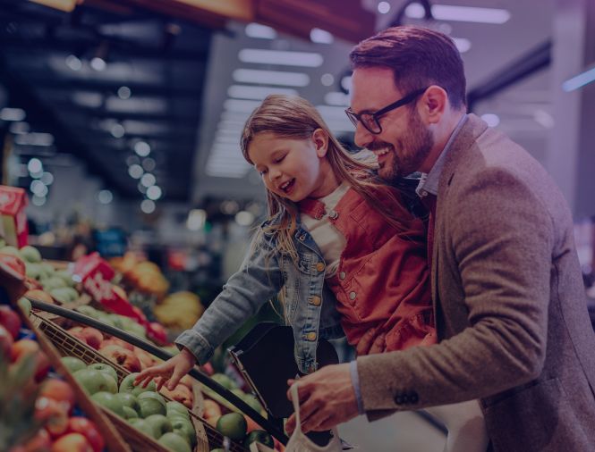 A father holding his daughter pick out fresh produce at the store