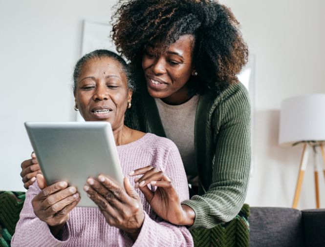 Two smiling Black women, one older and one younger, look at paperwork together