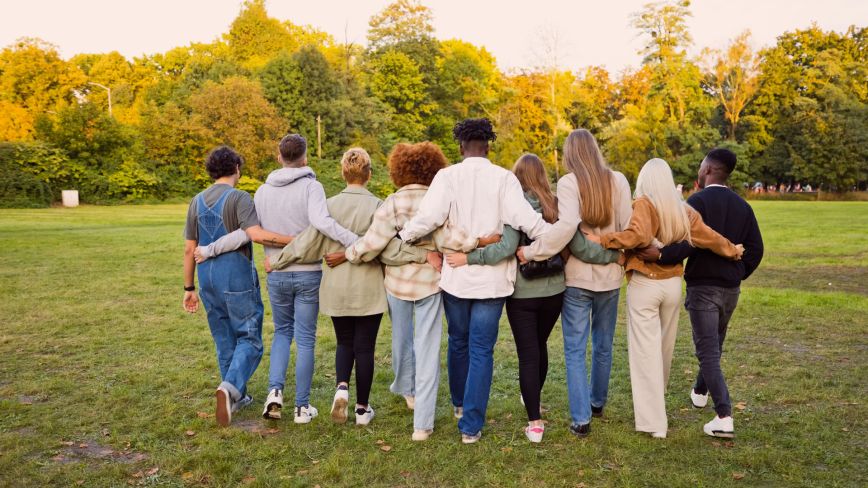 A group of people standing in a line with their arms around one another's backs, photographed from behind.