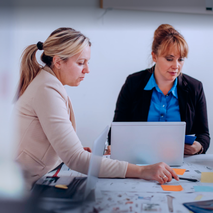 2 female adults are sitting around a conference room table with sticky notes collaborating