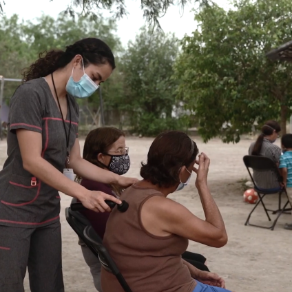 standing masked medical worker with a hand on the shoulder of a sitting woman