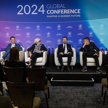 A set of six people sit on stage during an event panel