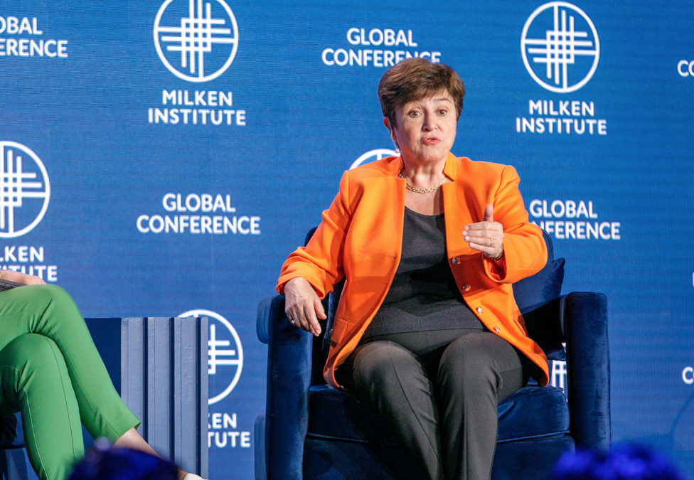 woman on stage sitting in blue chair speaking at Milken Conference