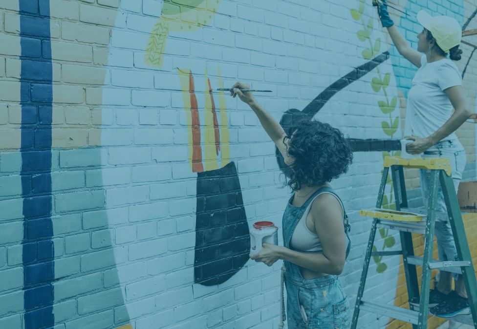 Two people painting a mural on brick wall