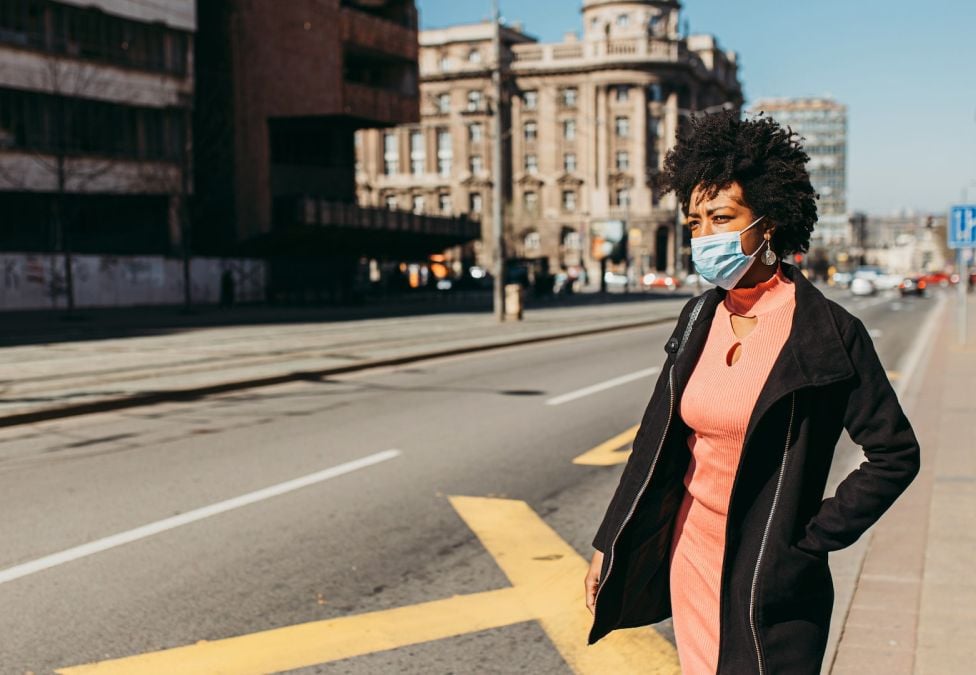 A young darker-skinned female stands on the sidewalk waiting to cross the street