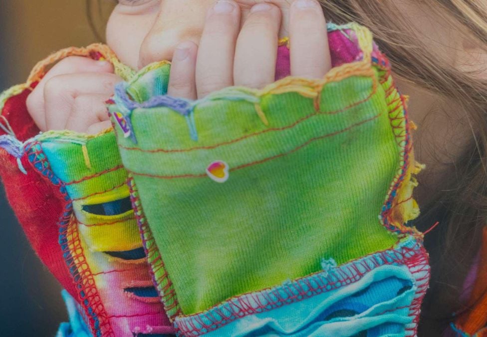 A child's hands by their face wearing a colorful long sleeve shirt