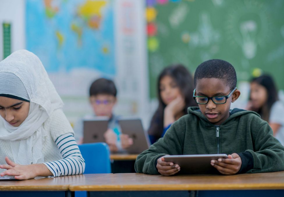 A few schoolkids sitting at their desks with tablets in their hands