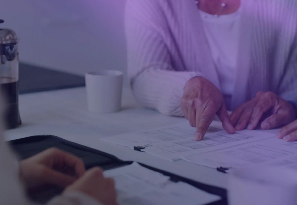 A person's finger points at a document on a desk.