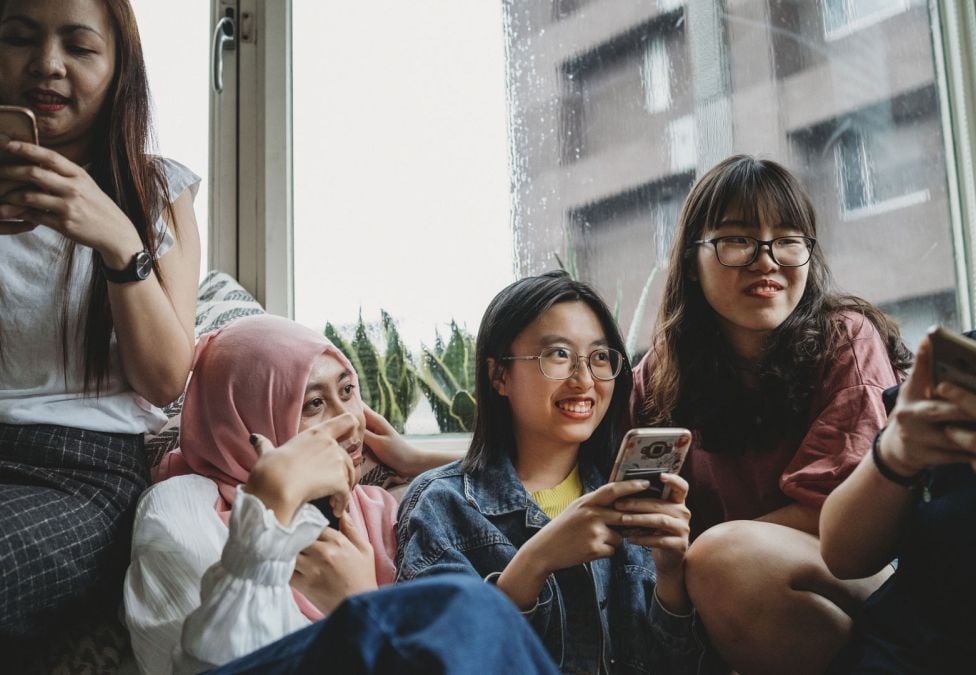 Five friends sitting together using their phones.