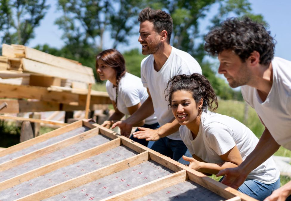 Four people erecting a wooden wall while building a house.