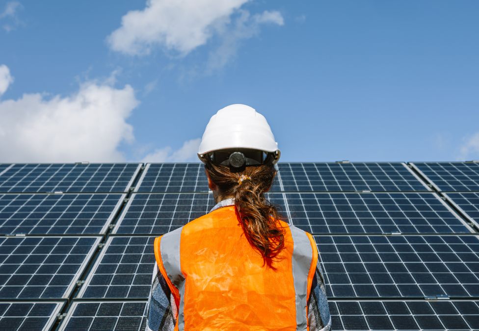 A person in a hardhat and hi-viz vest observes a large solar panel.