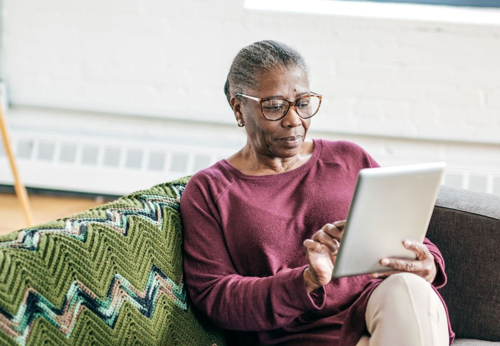 An elderly woman using a tablet while she sits on a couch.