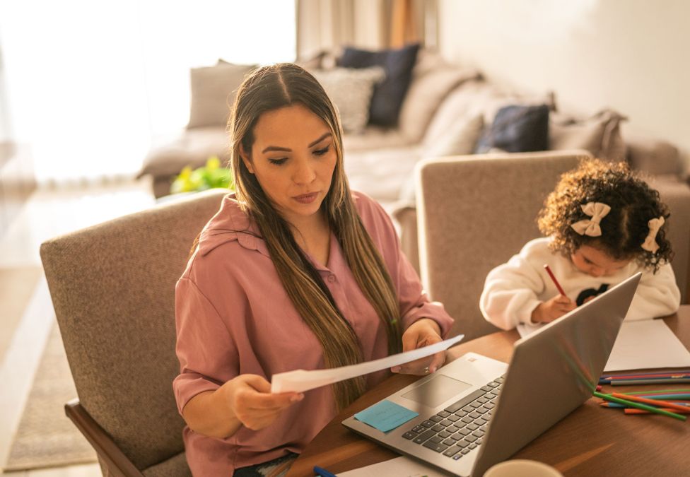 parent at laptop with child on side writing something and looking down