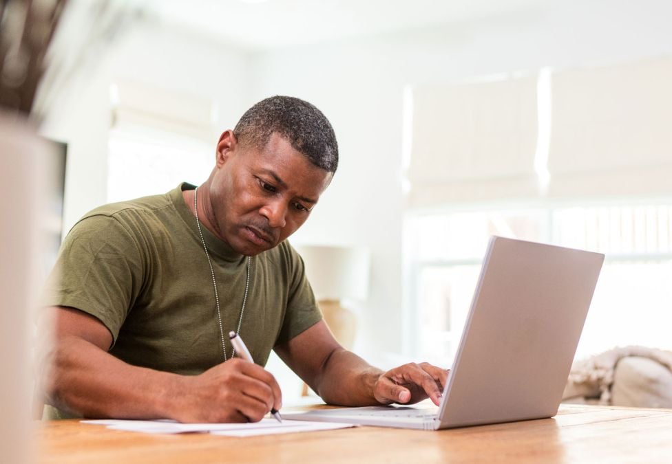 person at laptop and writing at desk