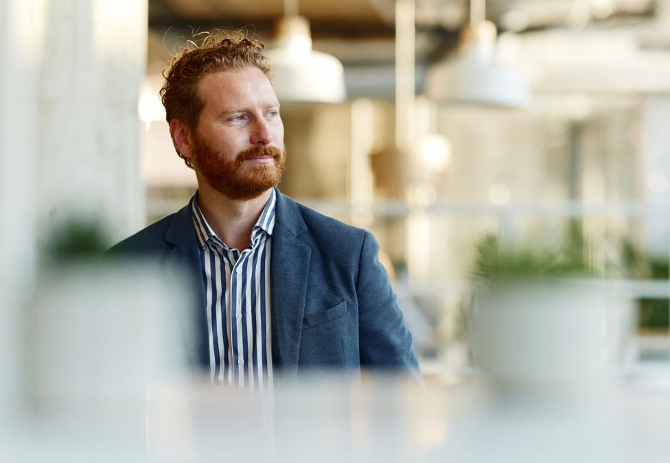 A man with red hair and beard wearing a suit looking left