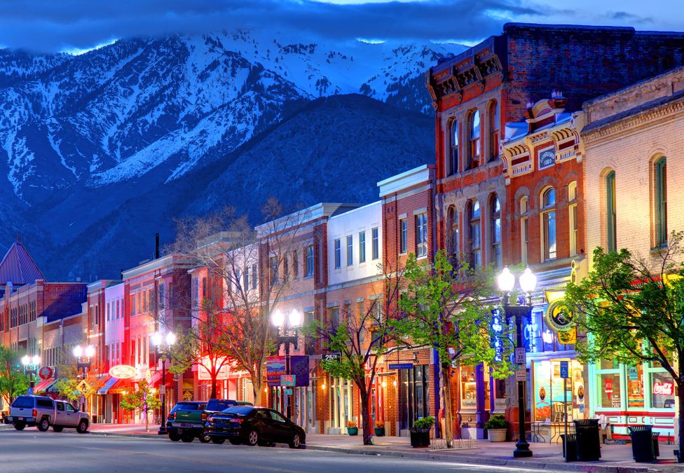 A city street with low-rise connected buildings lining the street and a snowy mountain background, leading to an article titled "The Rise of Mid-Sized American Cities: The Drivers of Perfectly-Sized Growth"