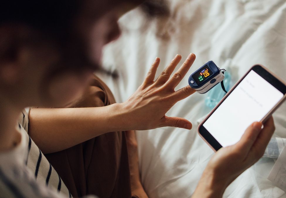 Image of a person's hands who is using a pulse oximeter and reading the results on a smart phone, acting as a hero image for an article about self-sustaining models for preventative health investments